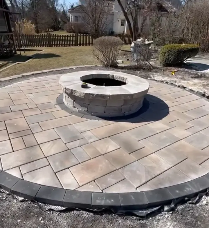 A circular paver patio around a stone fire pit, edged with a dark border course
