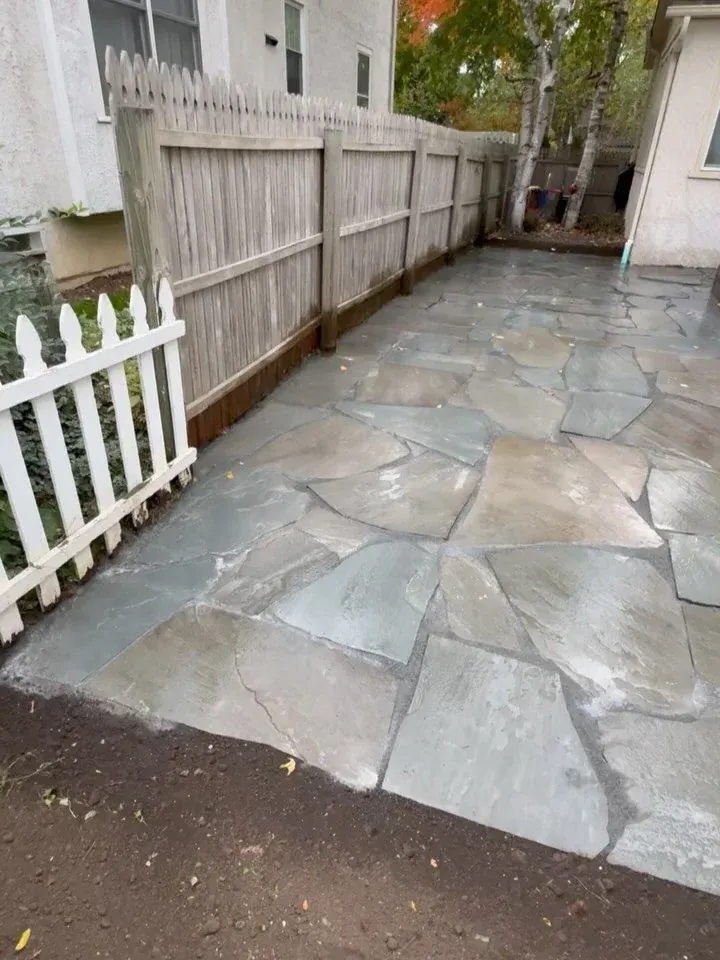 A flagstone patio laid along a wood fence and a white picket gate